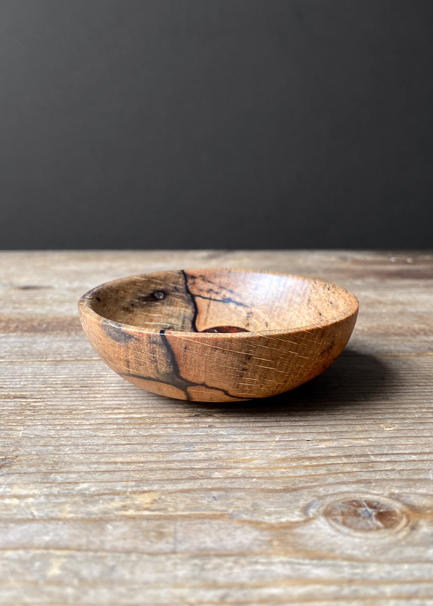 Small Spalted Beech wooden bowl on wood table against dark background.