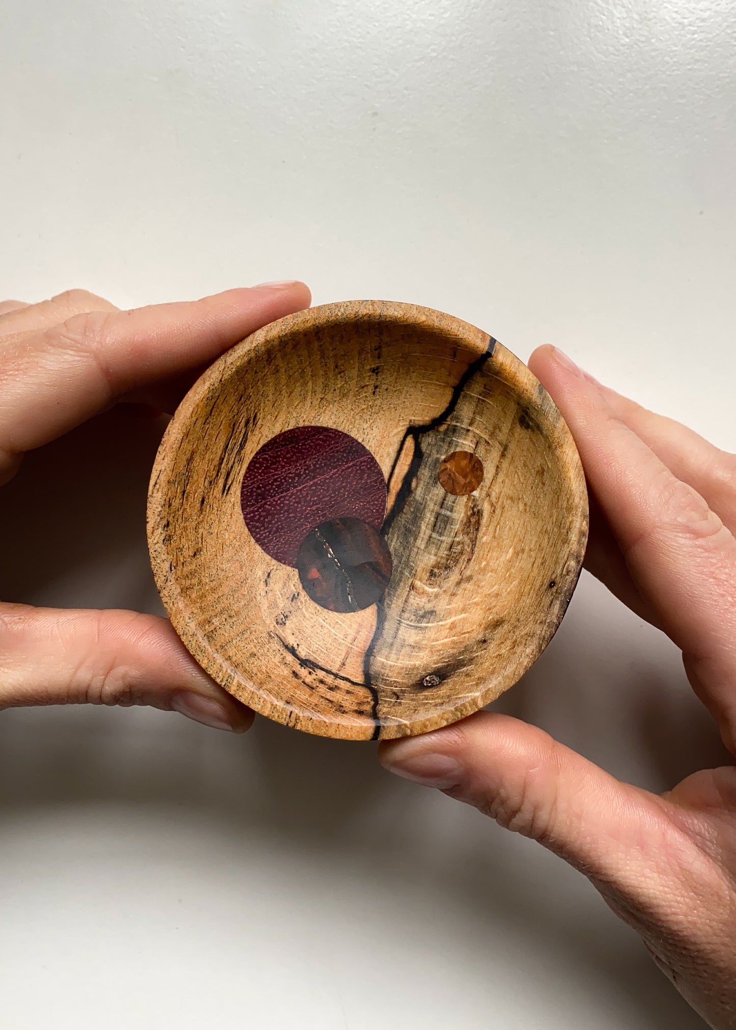 Small Spalted Beech bowl with circular wooden inlays held in hands against white background.