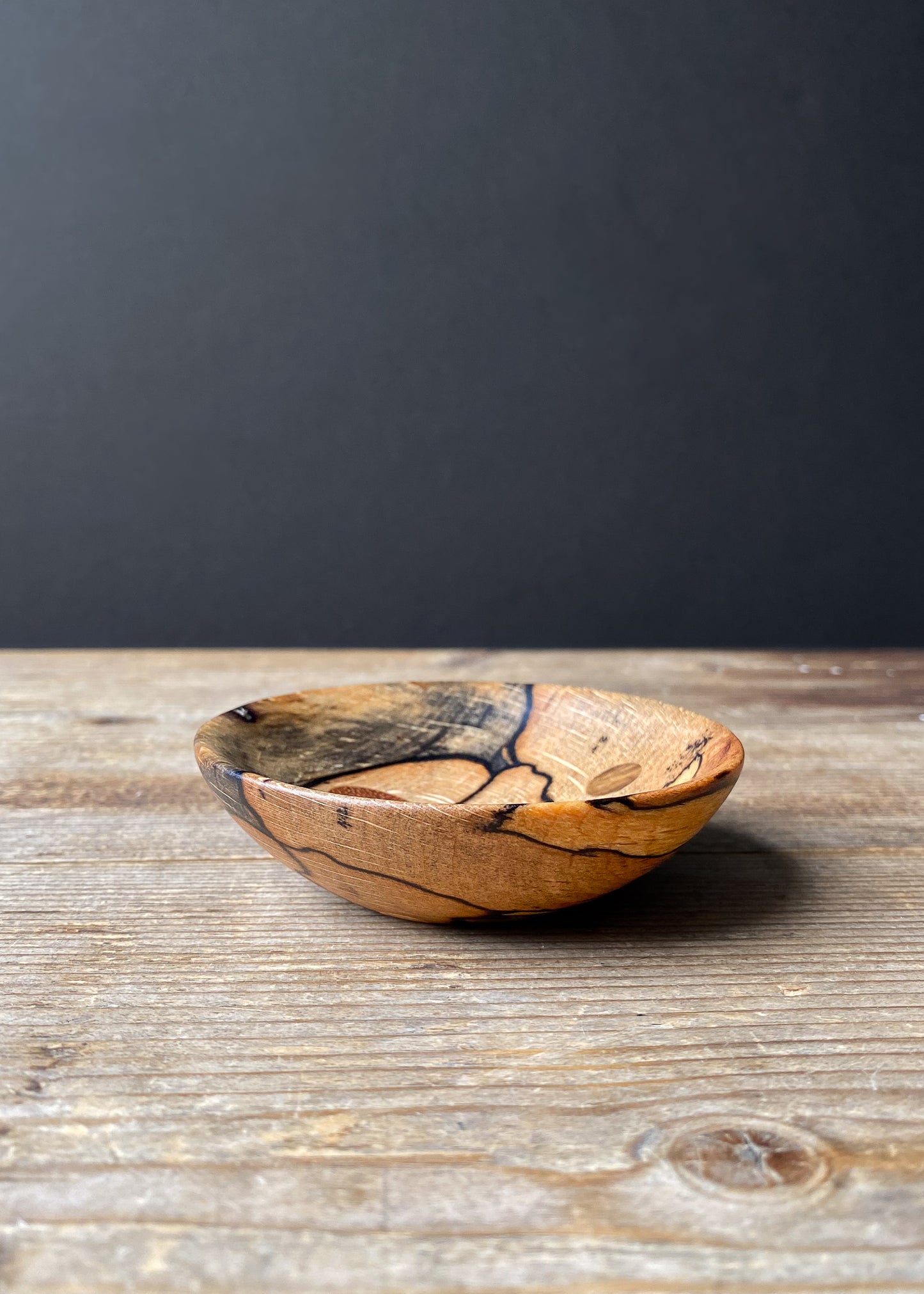 Shallow Spalted Beech wooden bowl on wood table against dark background.