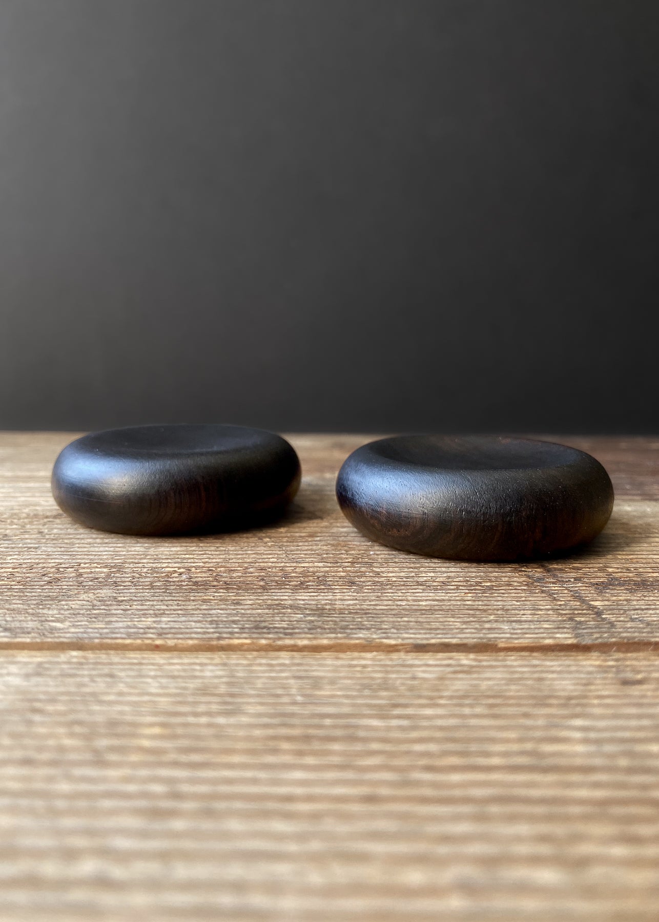 Two mini black wooden plates on wood table with black background.