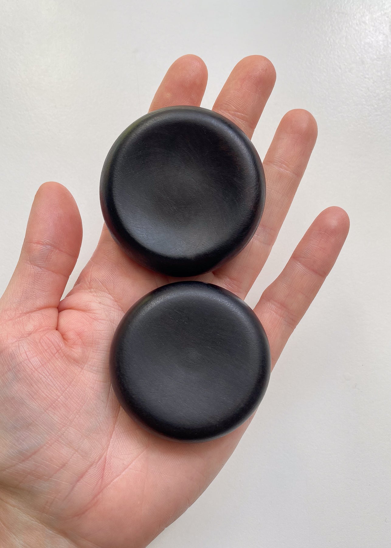 Two small black wooden plates in an open hand with white background.