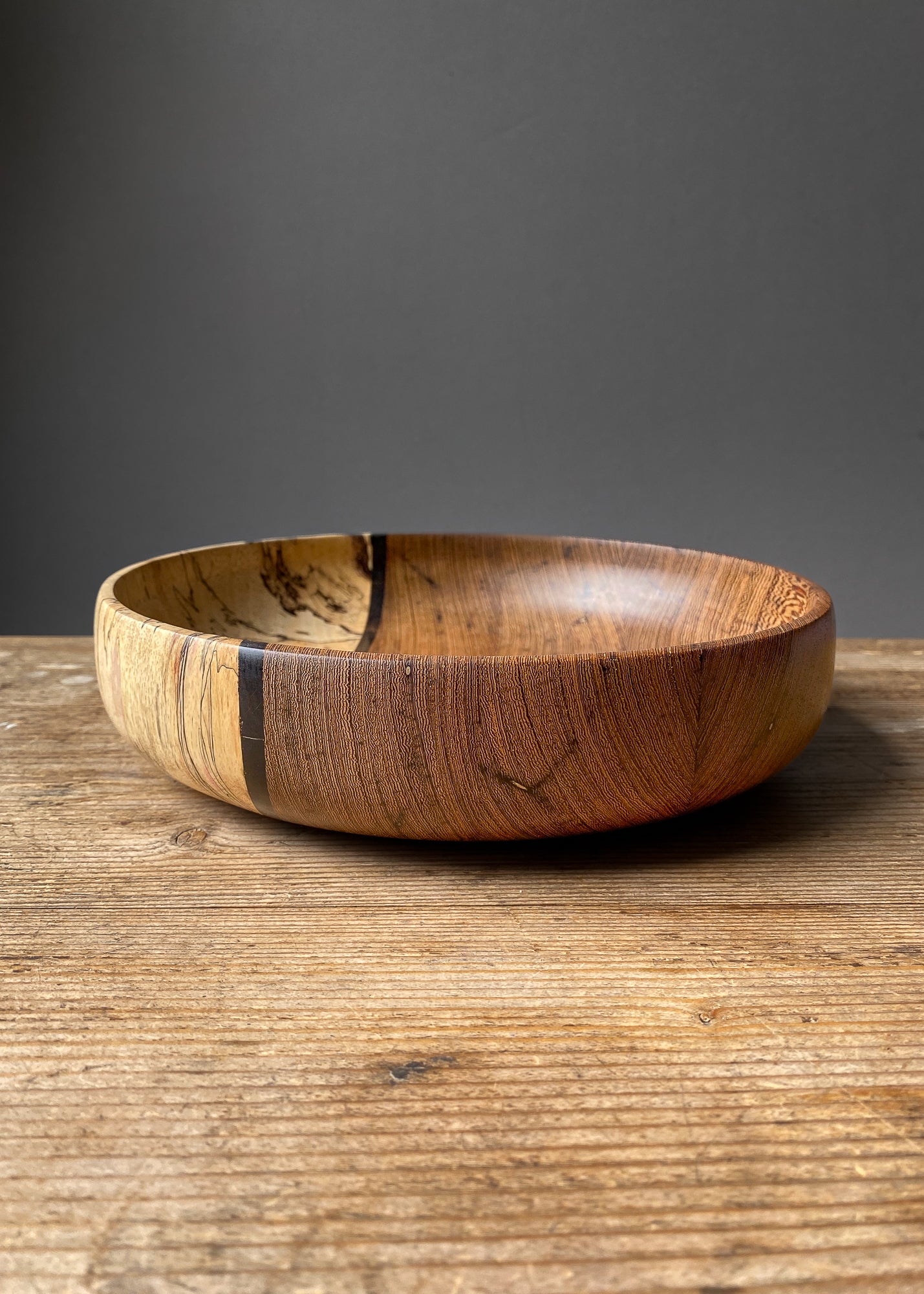 Large brown and spalted segmented wooden fruit bowl on wood table.