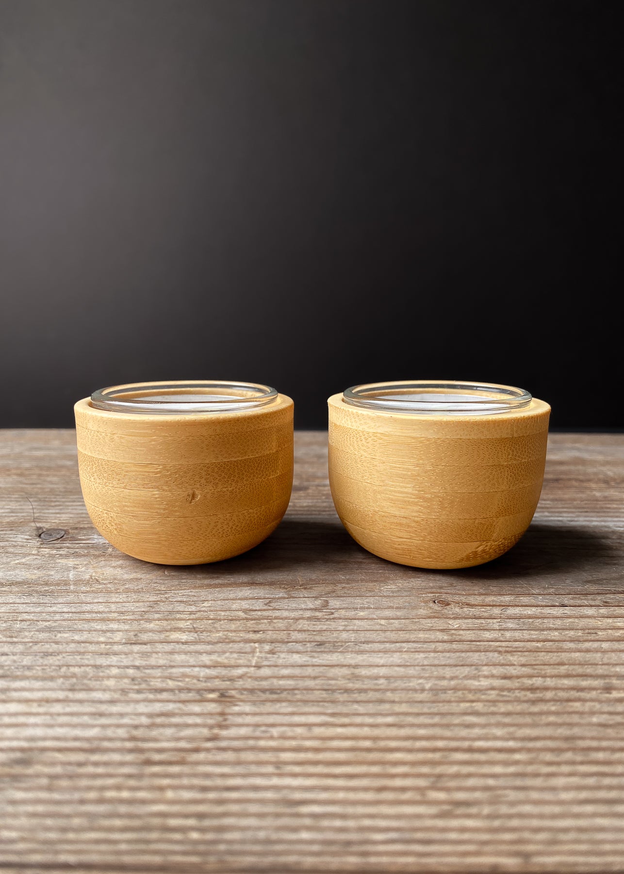 Set of two bamboo candle holders with clear glass inserts on a dark background.