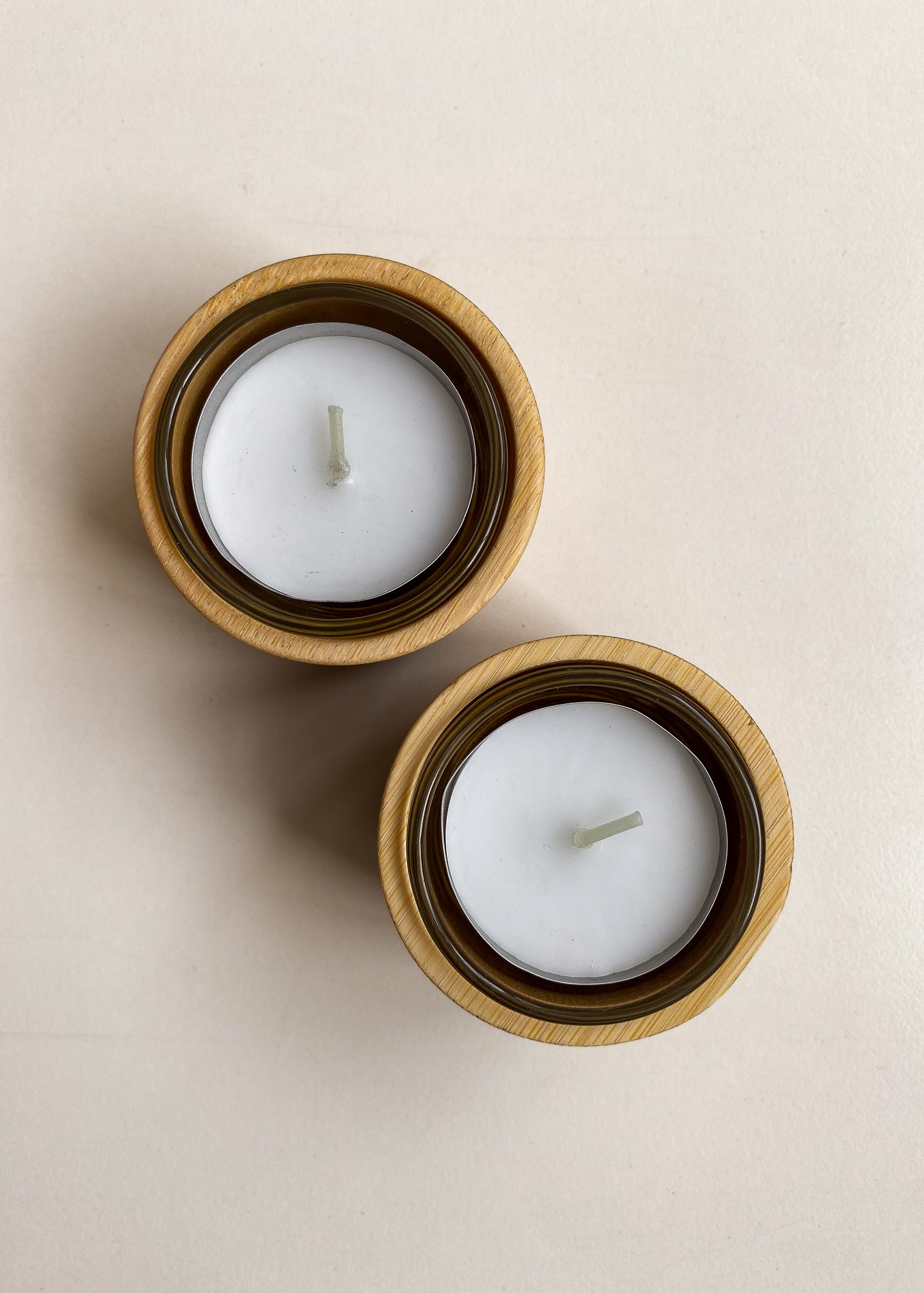 Overhead view of bamboo candle holder set with glass inserts and tea light candles on a white background.