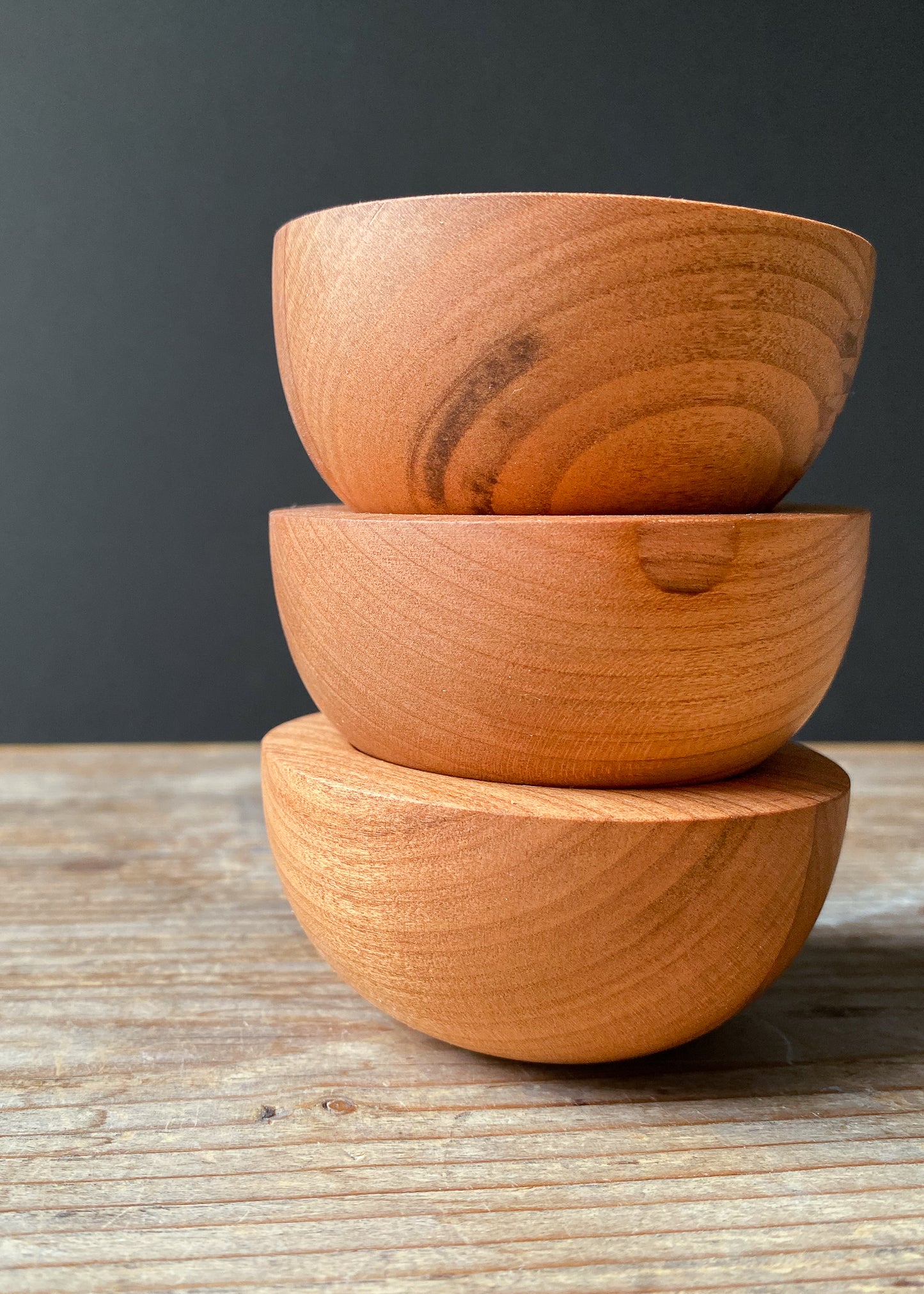 Set of three stacked rounded cherry wood candle holders on a dark background.