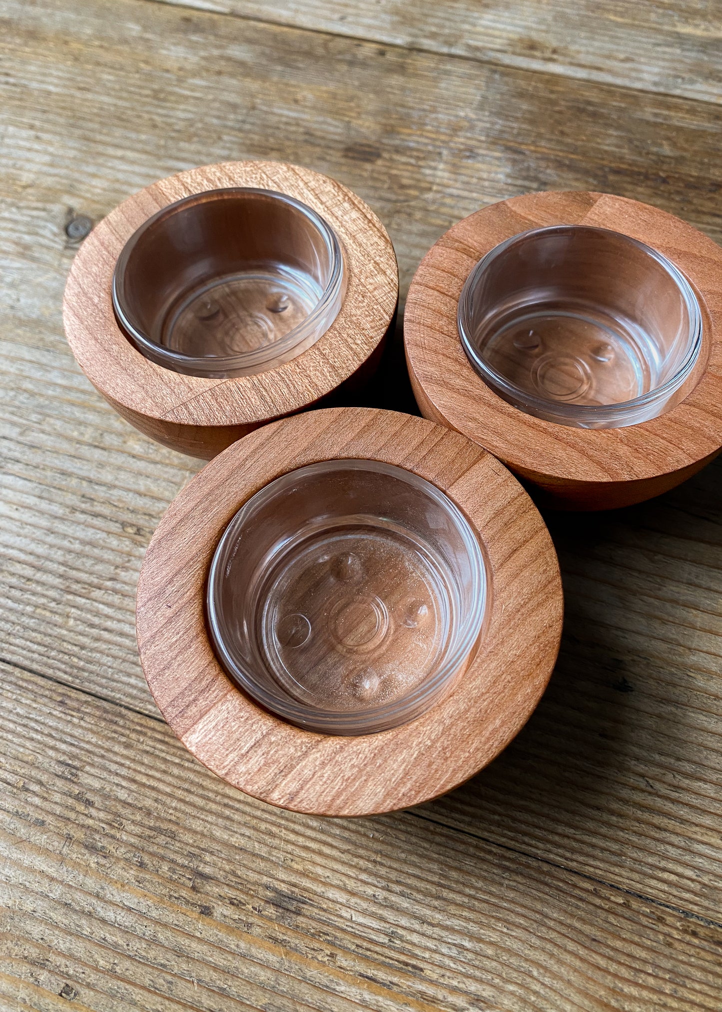Three rounded cherry wood candle holders with glass inserts on a wooden table.