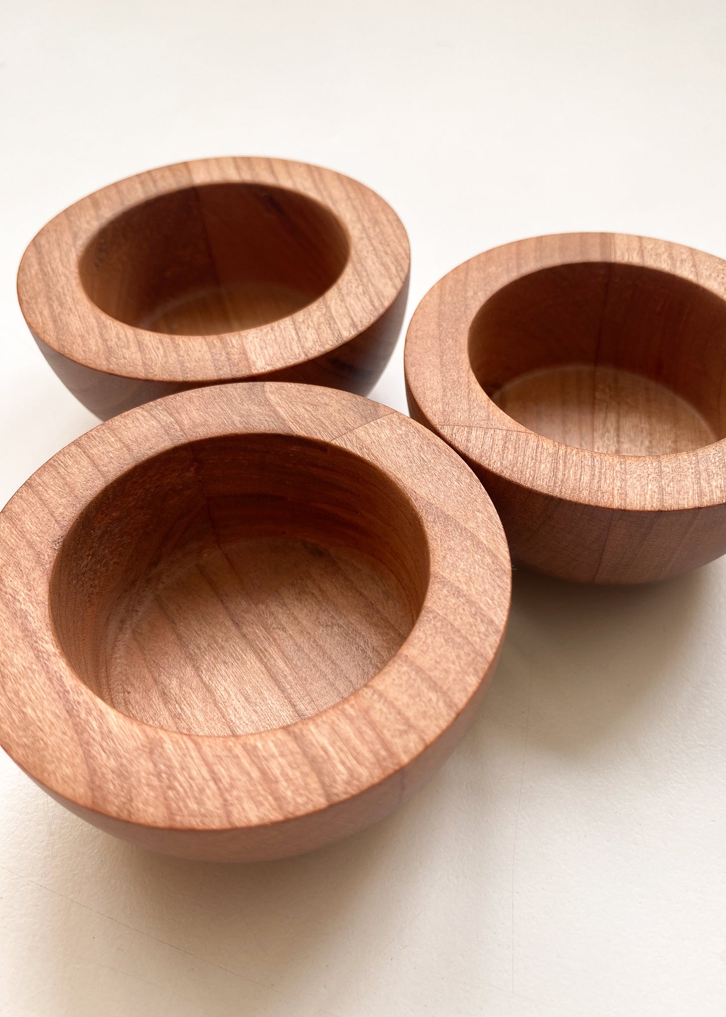 Close-up of three rounded cherry wood candle holders on a white background.