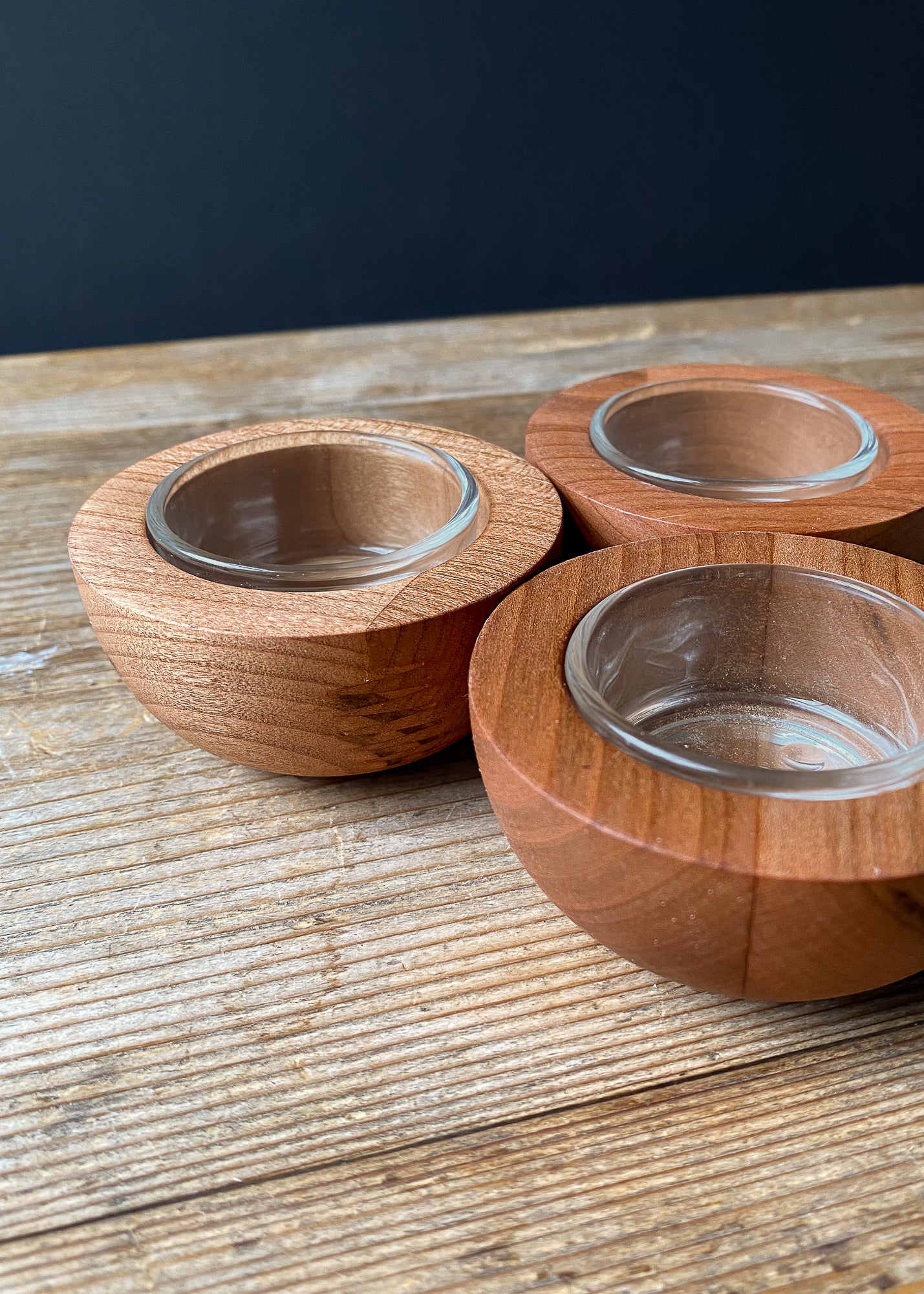 Three rounded cherry wood candle holders with glass inserts on a wooden table.