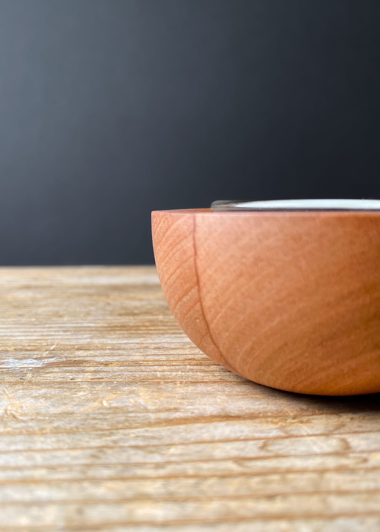 Close-up side view of a rounded cherry wood candle holder with a glass insert on a wooden table.