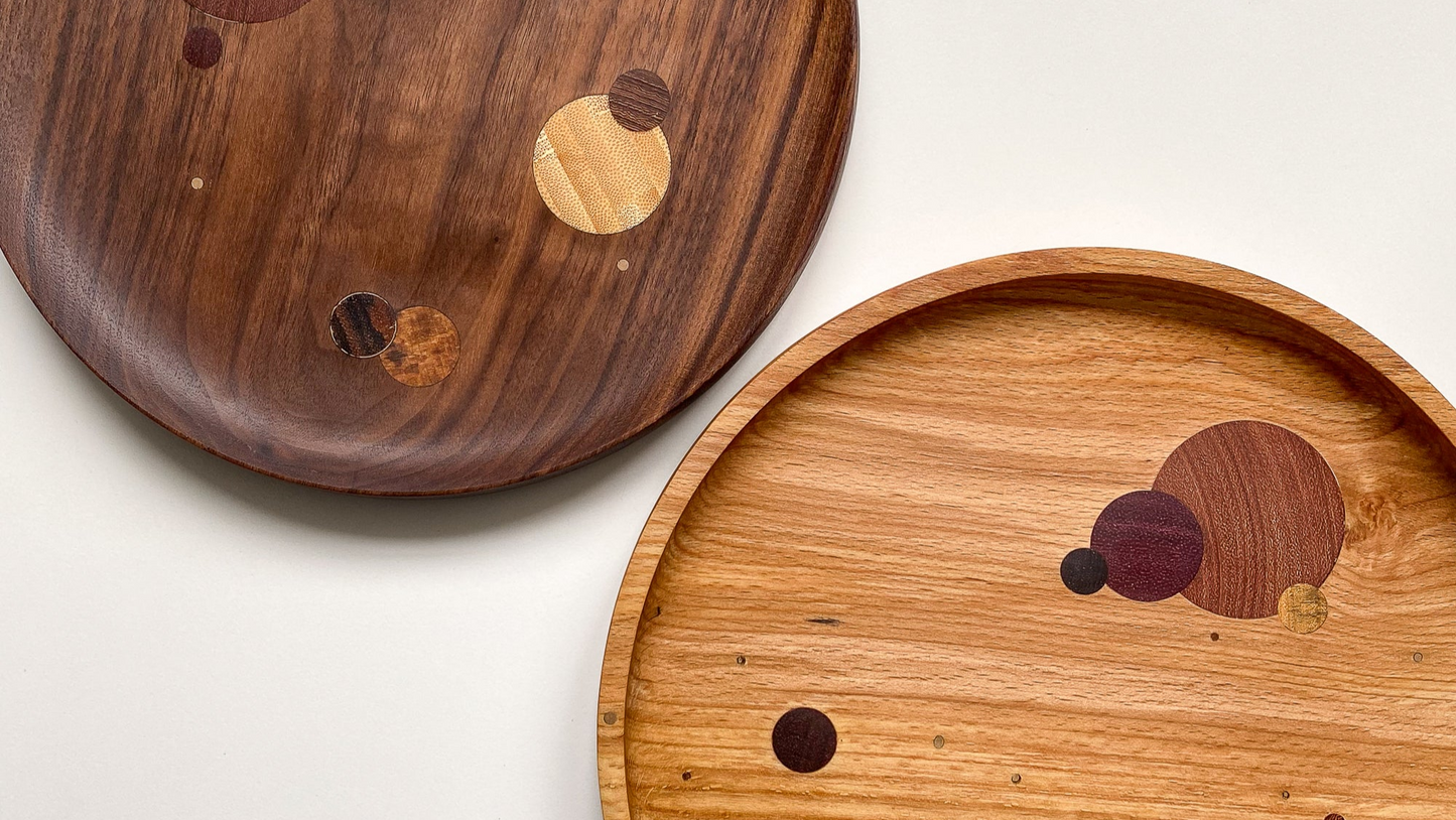Overhead view of two large wooden plates made from Walnut and Spalted Beech featuring round wooden inlays against white background.