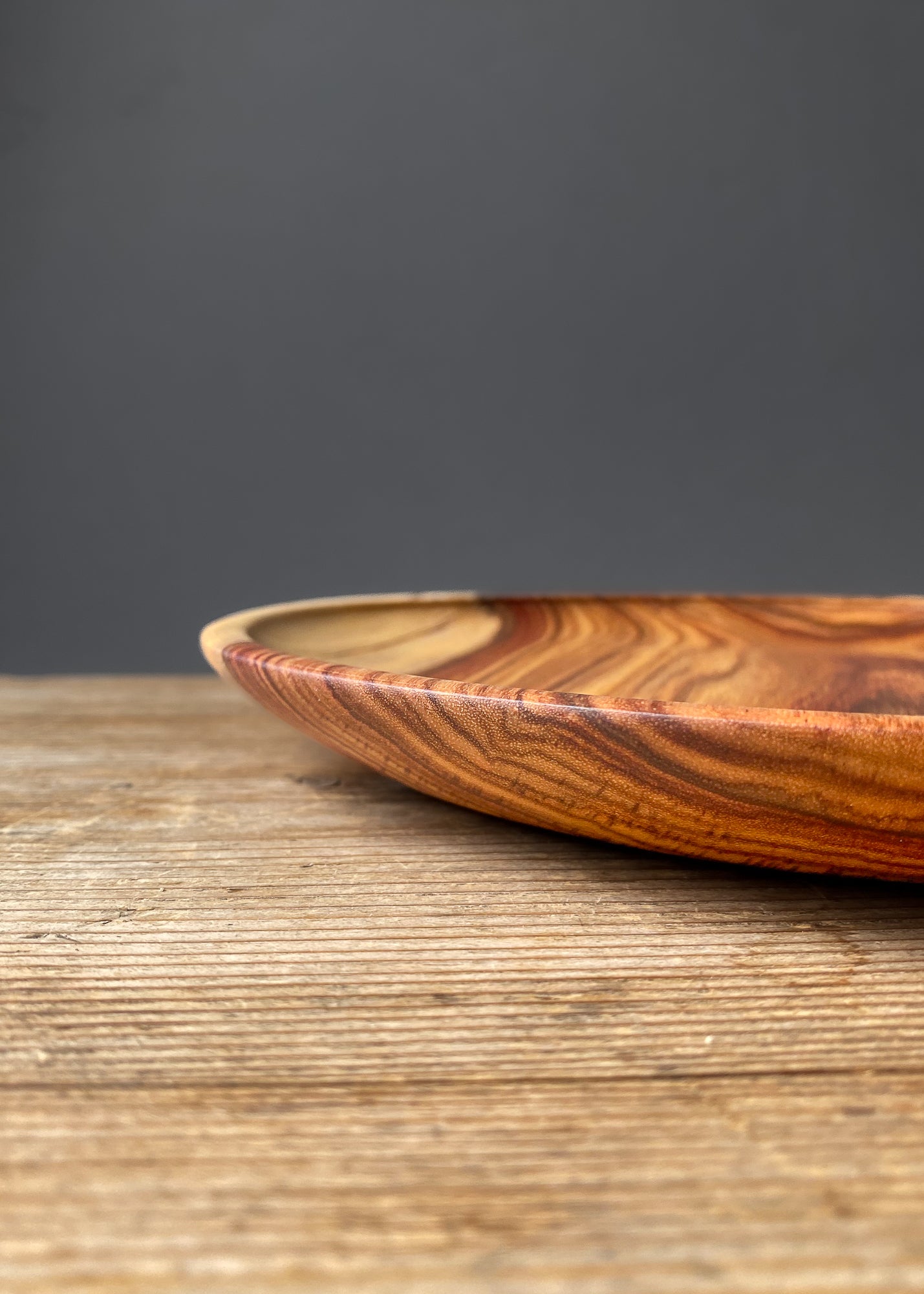 Side profile of large orange wooden tray on wood table with black background.
