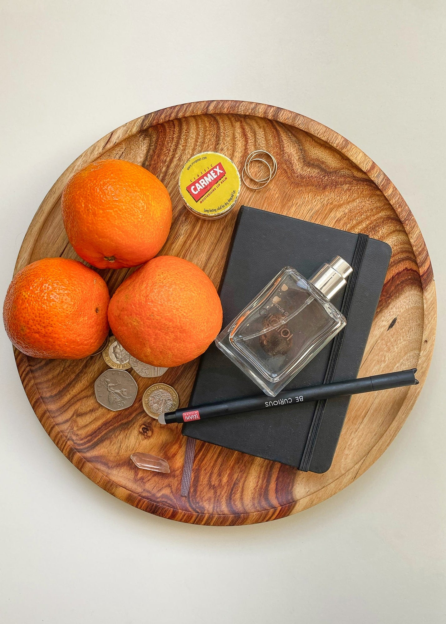 Top view of patterned orange wooden tray with fruit, jewelry, note pad and perfume bottle on white background.