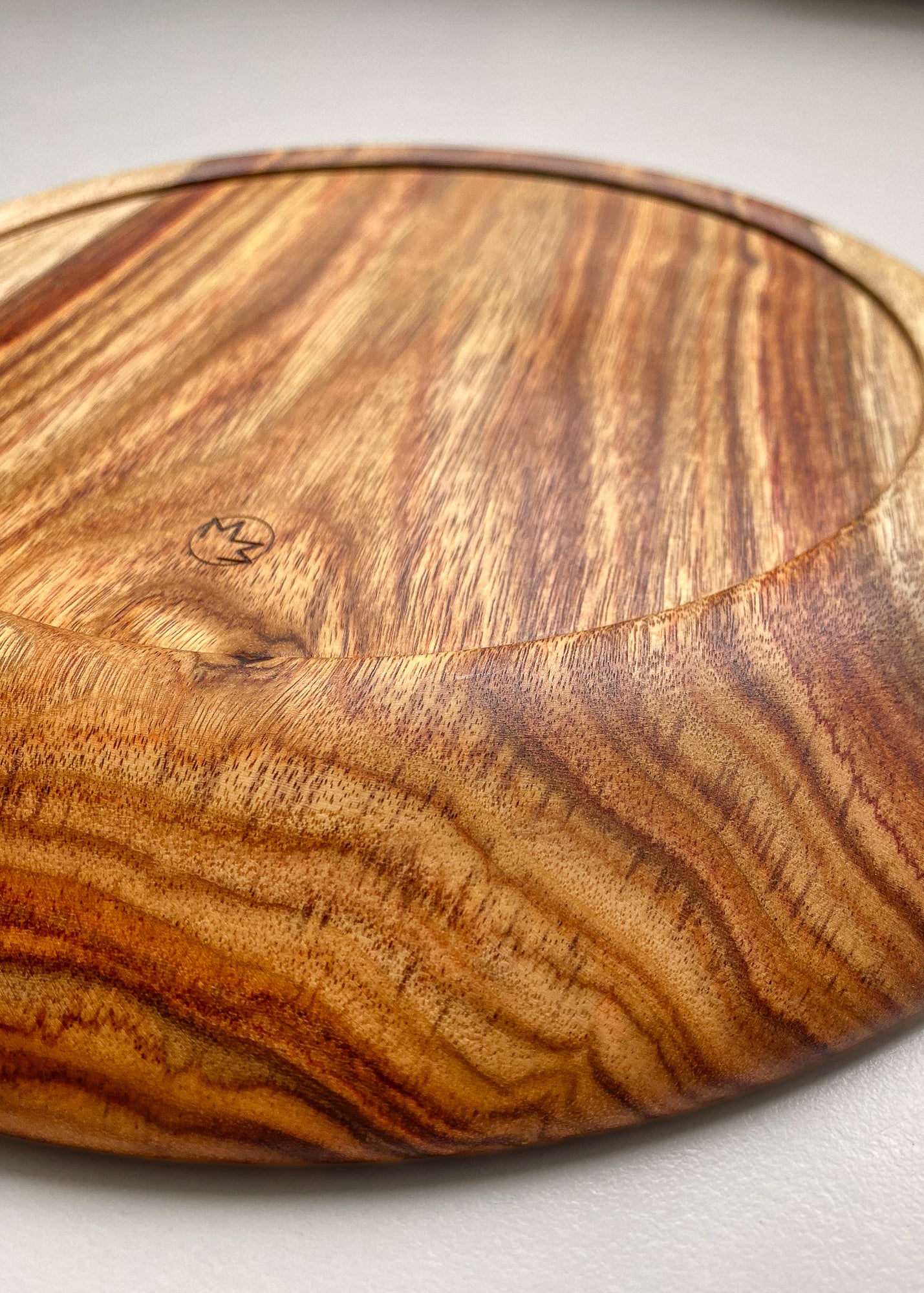 Underside close-up of orange wooden tray showing engraved logo on white background.