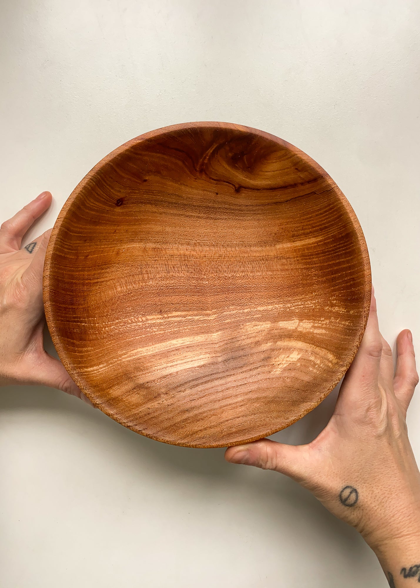 Overhead view of Elm wood fruit bowl held in hands on white background.