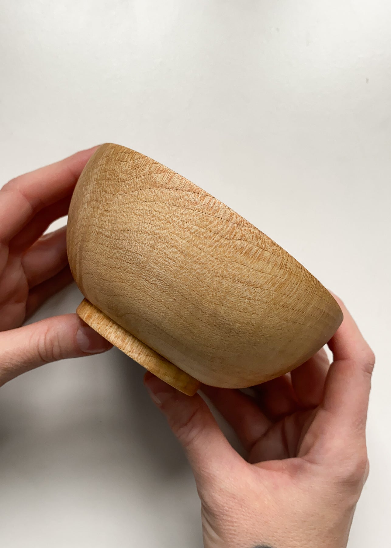 Side view of small sycamore wood bowl held in hands on white background.
