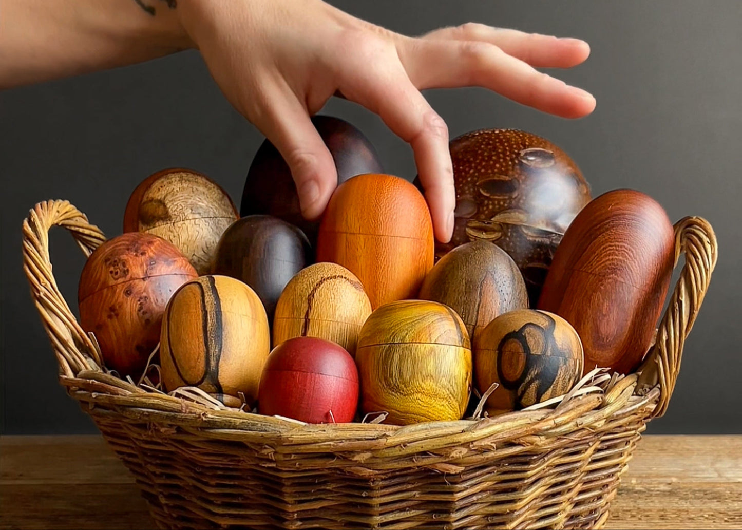 Hand reaching into a basket of colourful wooden egg shaped boxes with a dark background