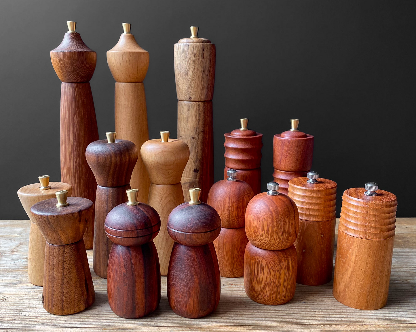 Collection of wooden pepper mills on a wooden surface with a dark background