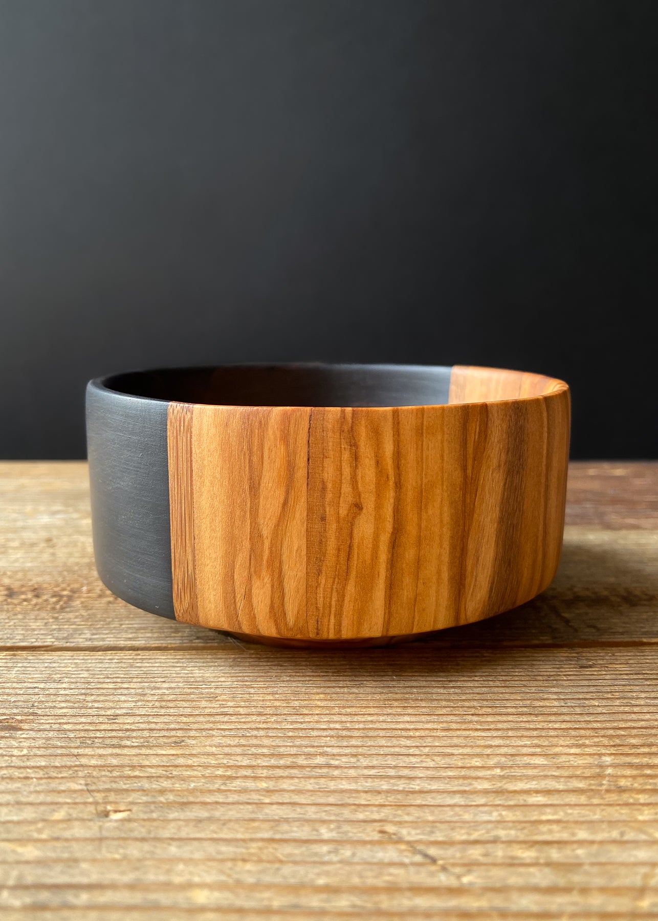 Segmented black and olive wooden bowl on wood table.