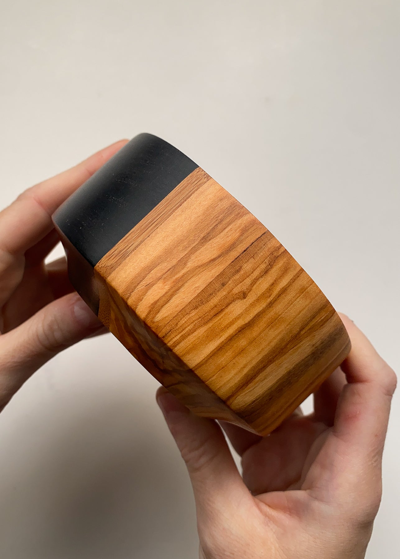 Side view of black and olive bowl held in hands on white background.