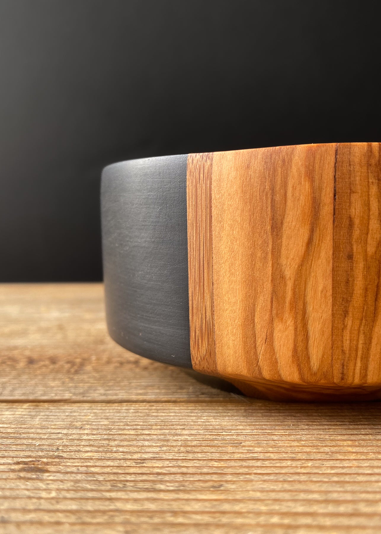 Close-up side detail of segmented olive and black wooden bowl on wood table.