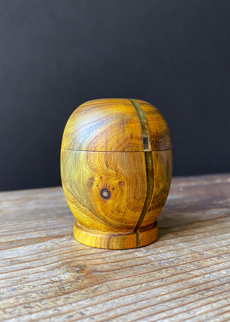 Small yellow patterned wooden box with resin strip on wood table.