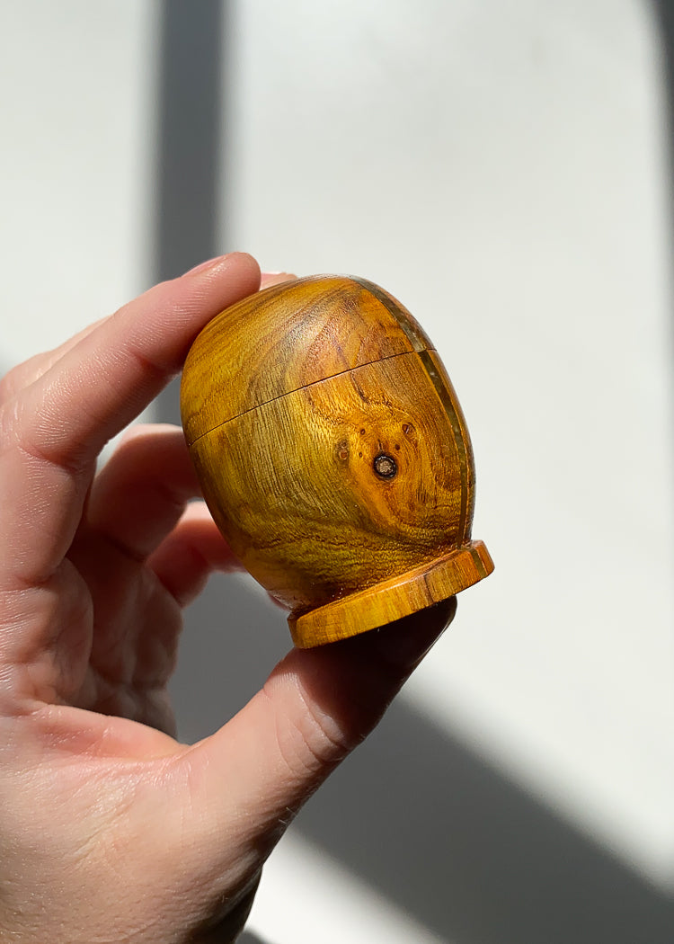 Small yellow patterned wooden box held in hand in natural light against white background.
