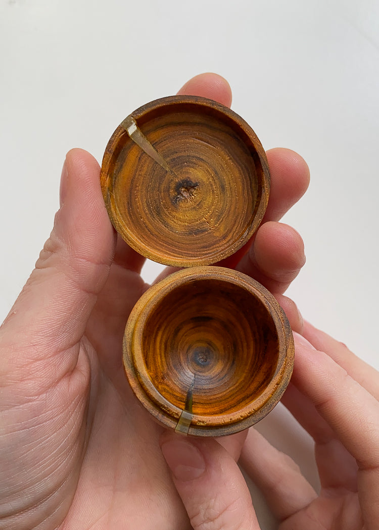 Overhead view of small lidded Laburnum wood box held opened in hands against white background.