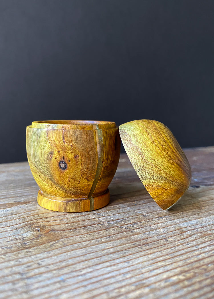 Small Laburnum lidded box on wooden table with lid open against dark background.