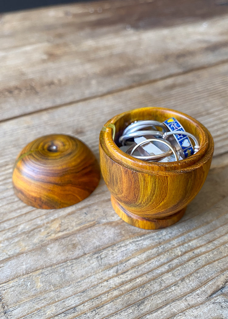 Detailed view of small orange and yellow wooden box on wood table with open lid displaying jewelry against dark background.