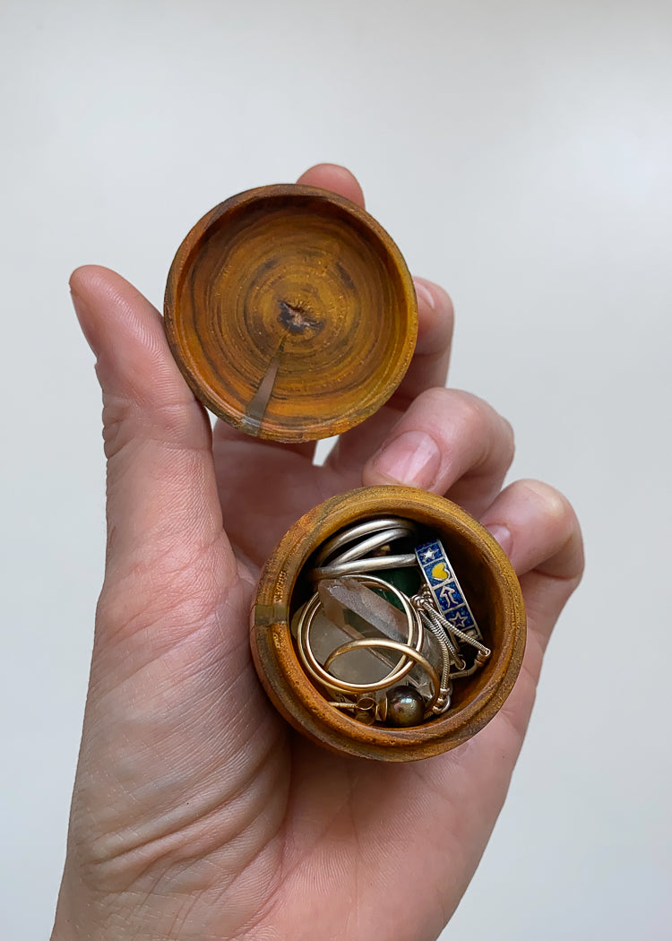 Small Laburnum and resin lidded box held opened in hand displaying jewelry against white background.