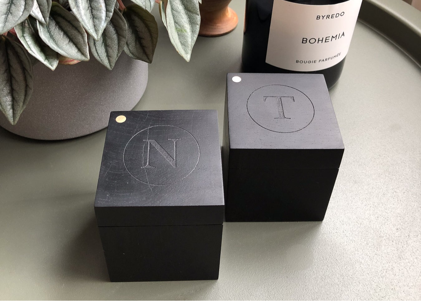 Two engraved African Blackwood boxes on table with plant and candle.