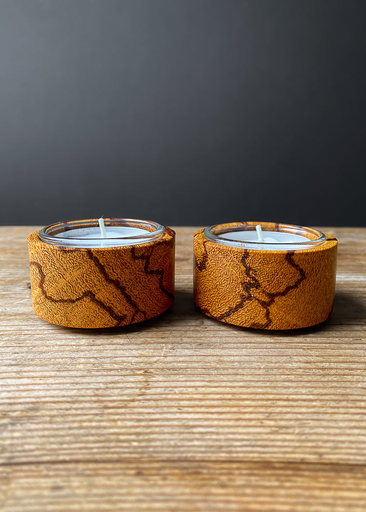 Side view of two Marblewood candle holders with glass inserts and tea light candles on wooden table.