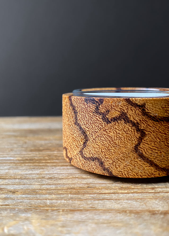 Close up side view of Marblewood candle holder with glass insert and tea light candle on wooden table.