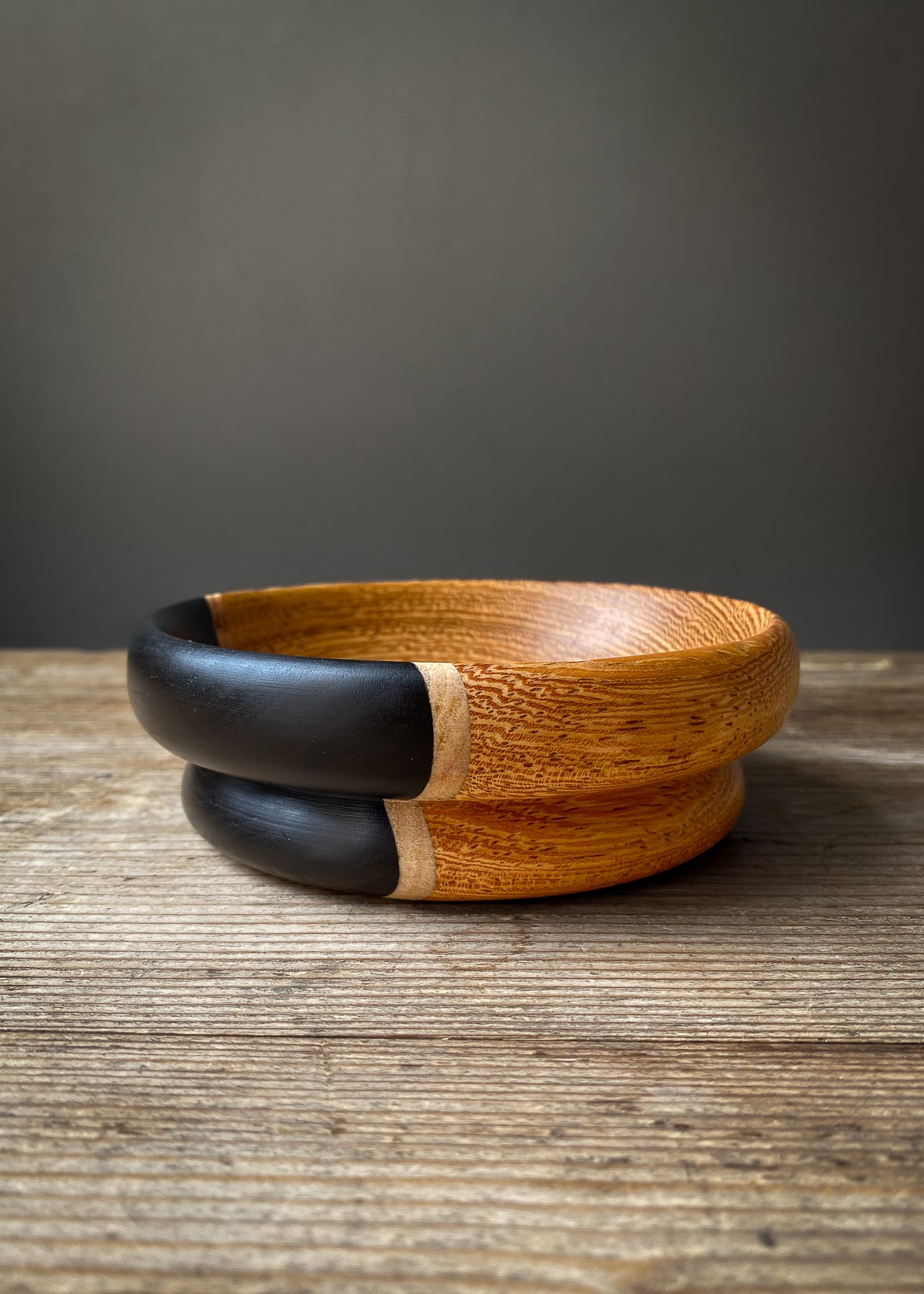 Rounded black and orange segmented wooden bowl on wood table.