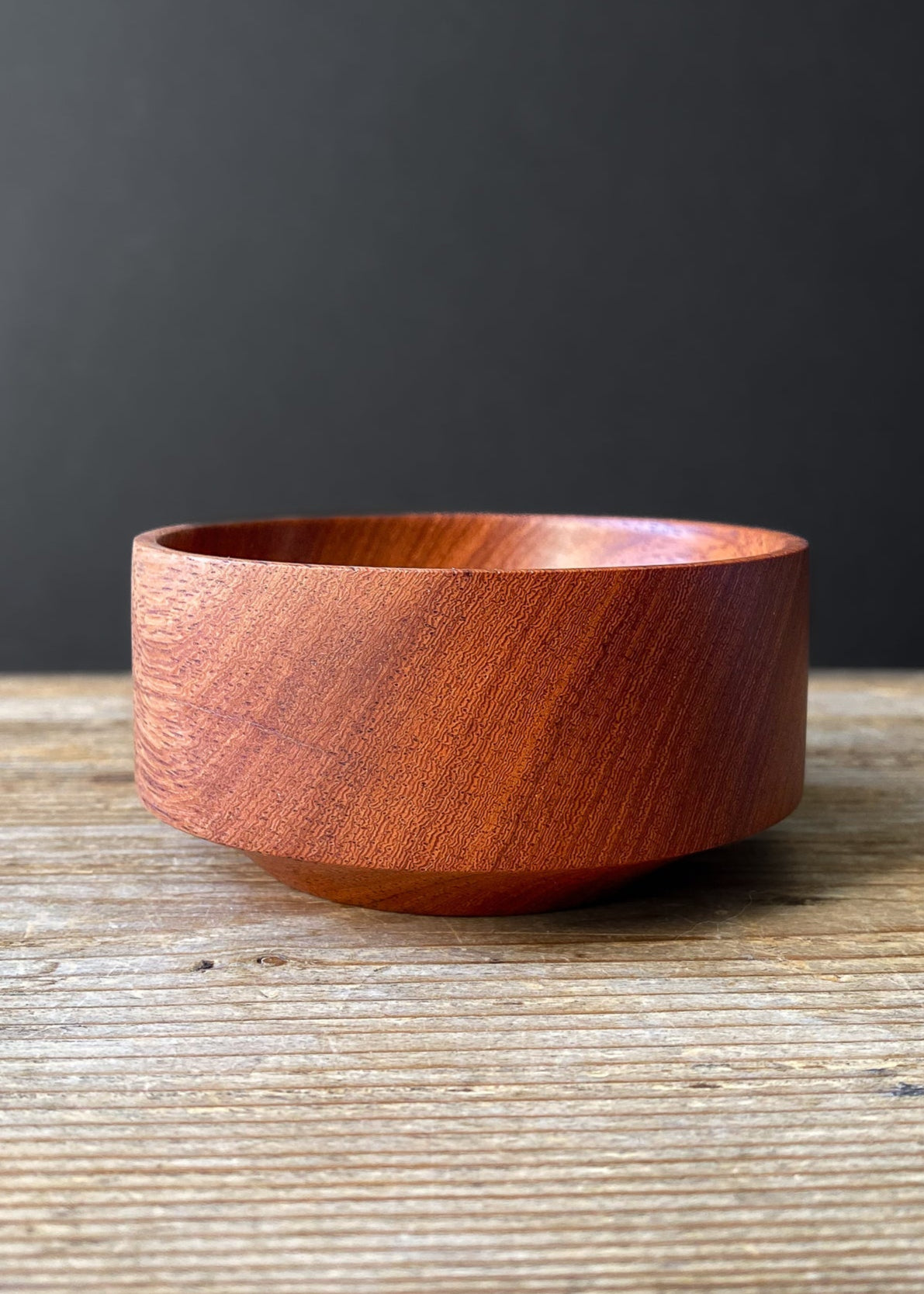 Small red orange wooden bowl on wood table with black background.