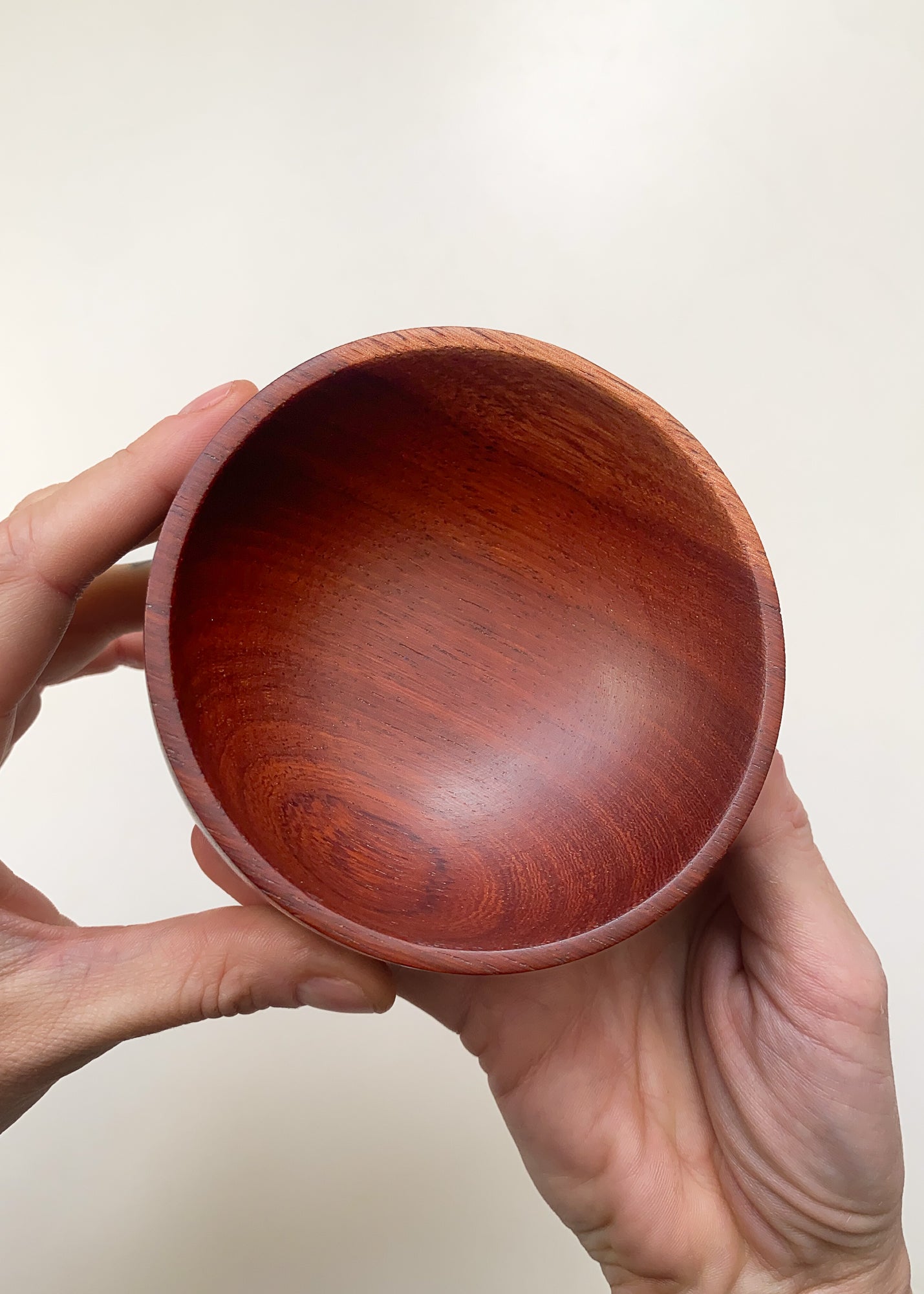 Reddish-brown wooden bowl held by a hand against a plain background