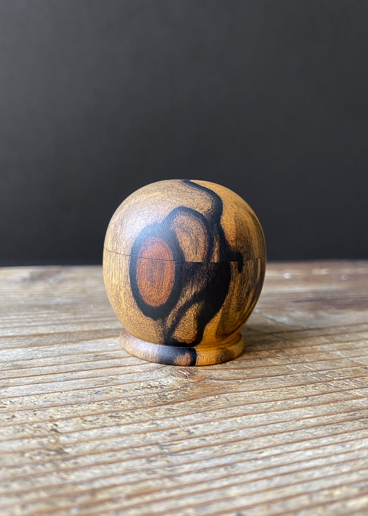 Mini wooden box with swirling black and orange patterns on wood table.