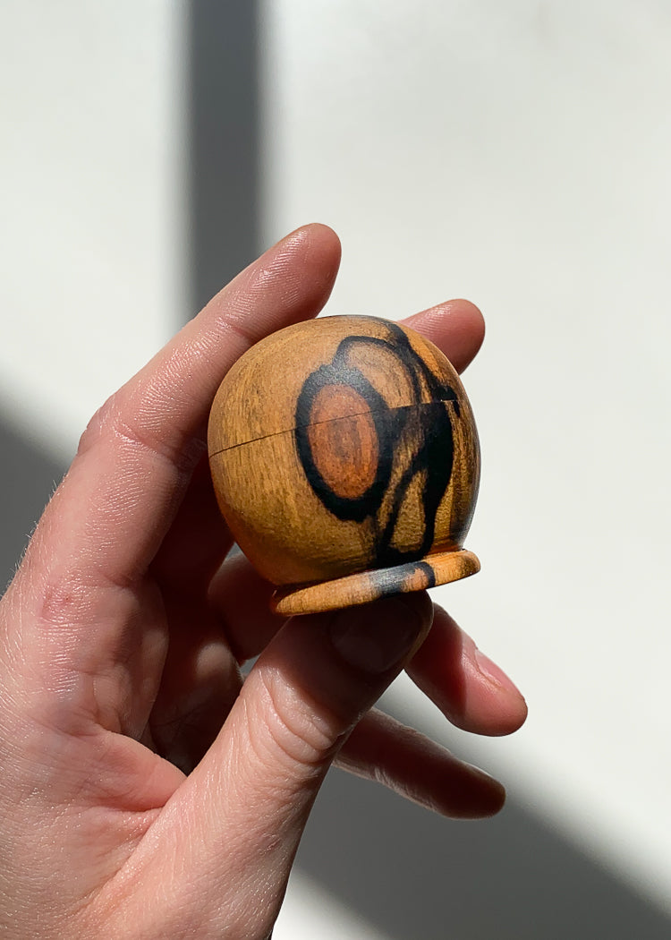 Small patterned black, orange and yellow wooden box held in hand in natural light against white background.