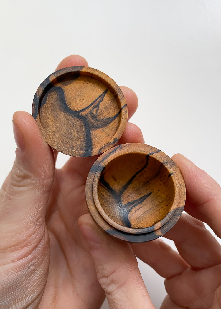 Overhead view of patterned orange and black wood lidded box held open in hands against white background.