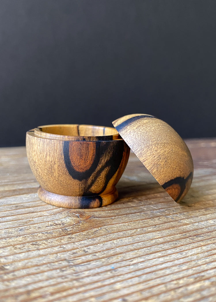 Side view of small patterned wooden lidded box on wood table with open lid.