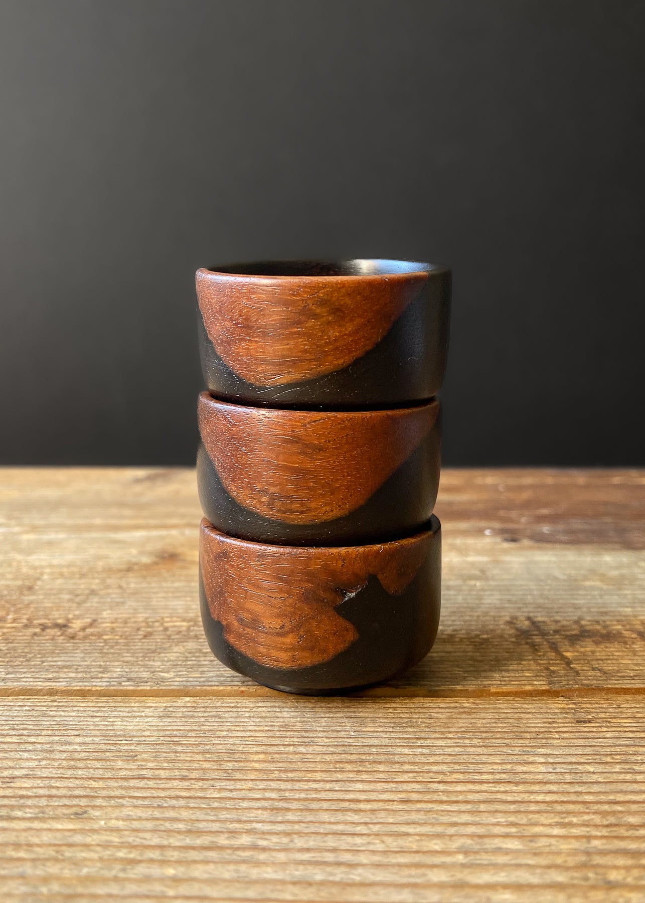 Three small black wooden bowls stacked on a wood table.