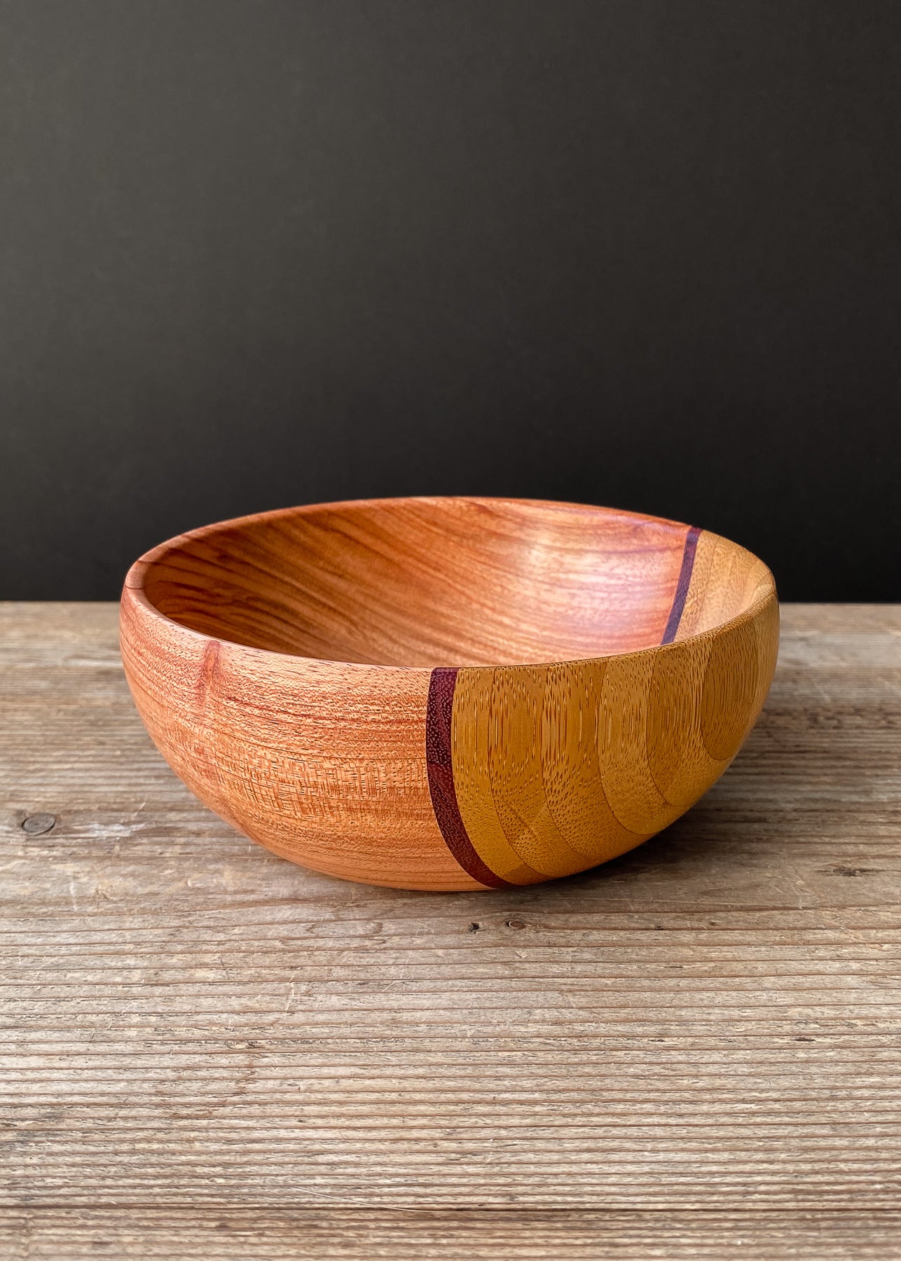 Segmented wooden bowl with purple strip on wood table.