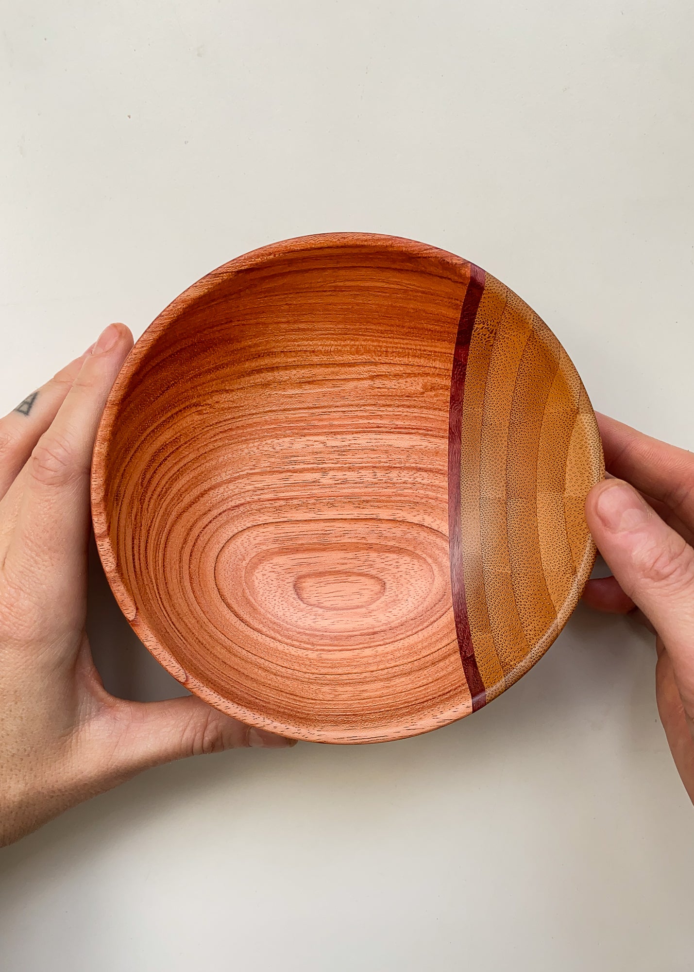 Top view of segmented wooden bowl held in hands on white background.