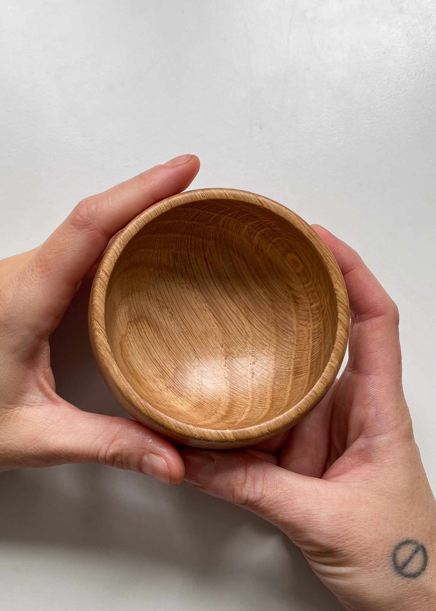 Top view of small Oak wood bowl held in hands on white background.
