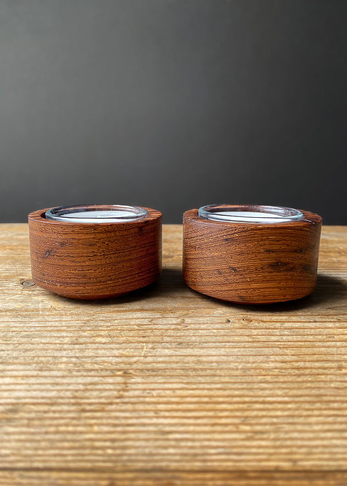 Side view of two Panga Panga candle holders with glass inserts and tea light candles on wooden table.