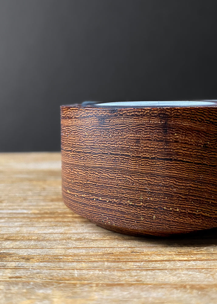 Close up side view of textured brown wooden candle holder with glass insert on wood table.