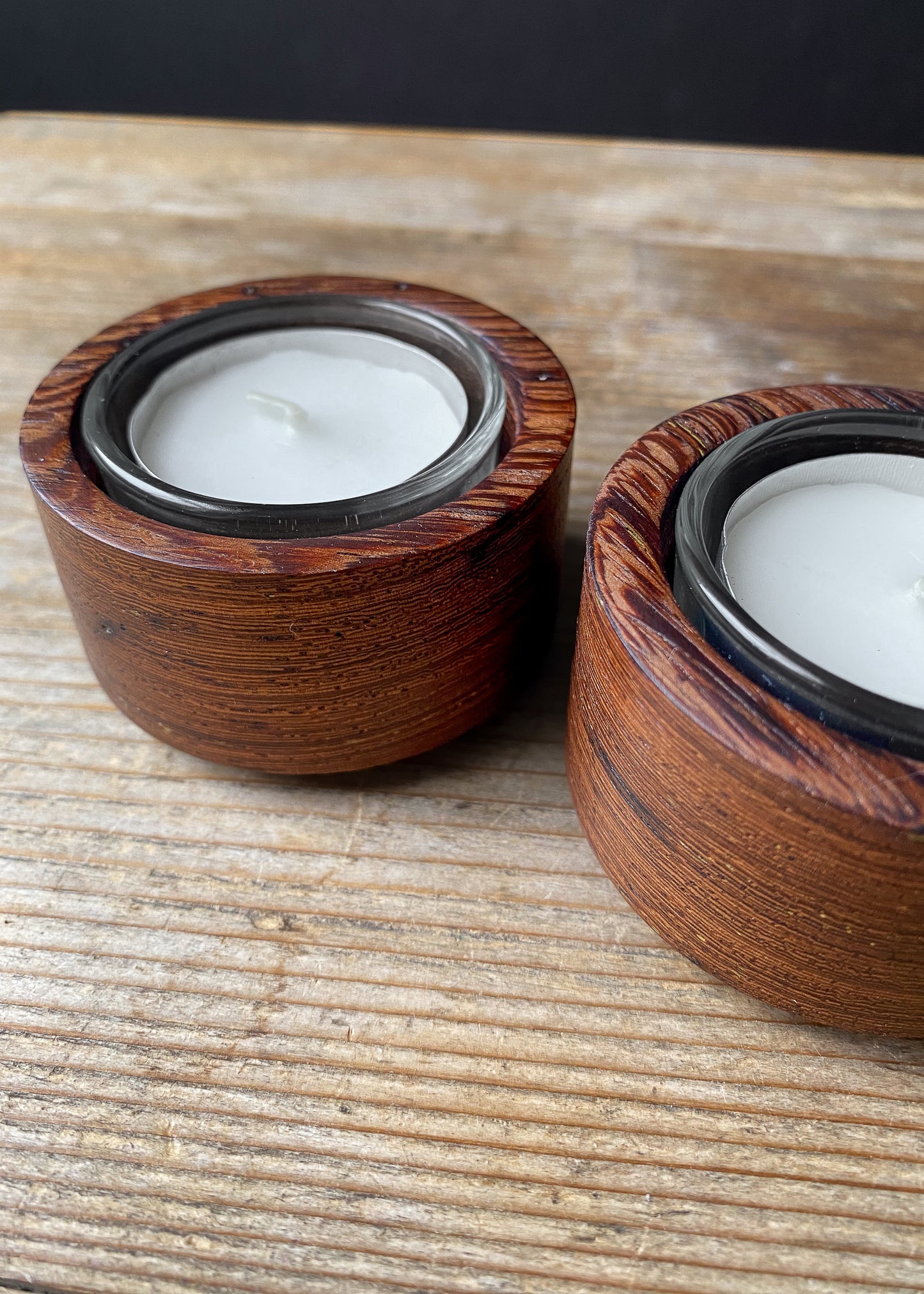 Close up inside view of two Panga Panga candle holders with glass inserts and tea light candles on wooden table.