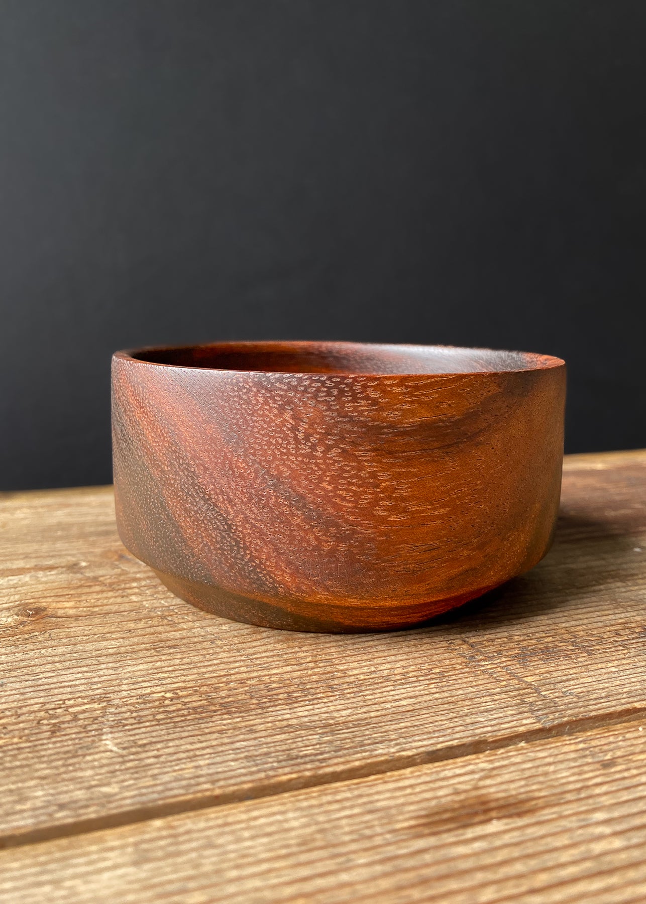 Brown Tanga Tanga wooden bowl on wood table with black background.
