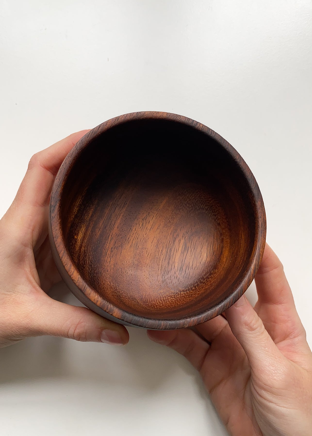 Tanga Tanga wooden bowl held in hands with white background.