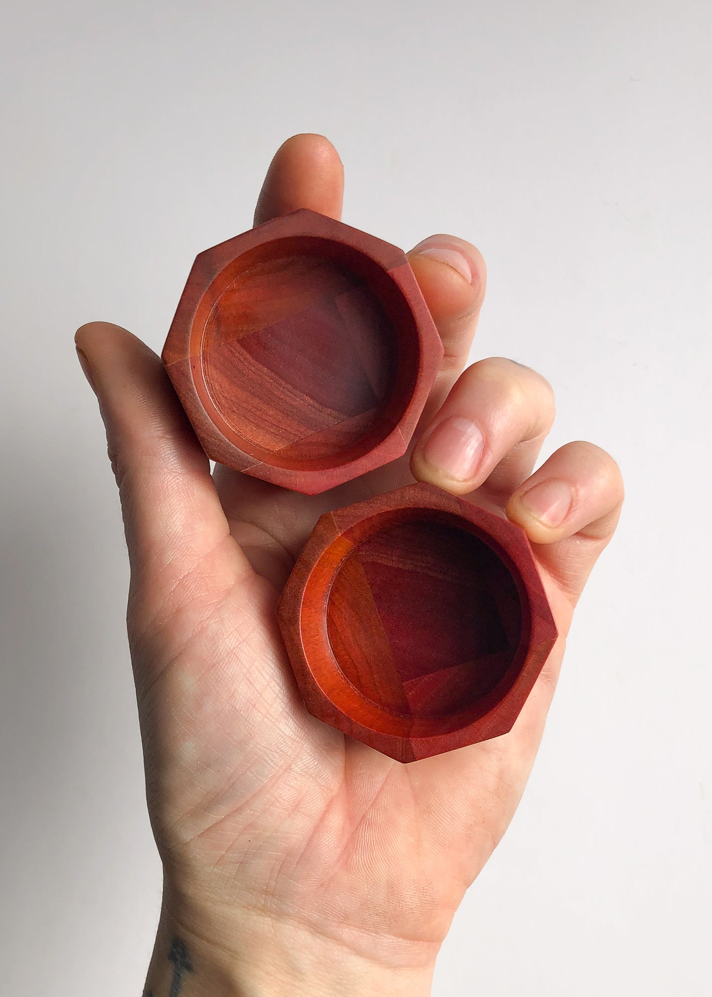 Hand holding two small pink octagonal wooden bowls on white background.